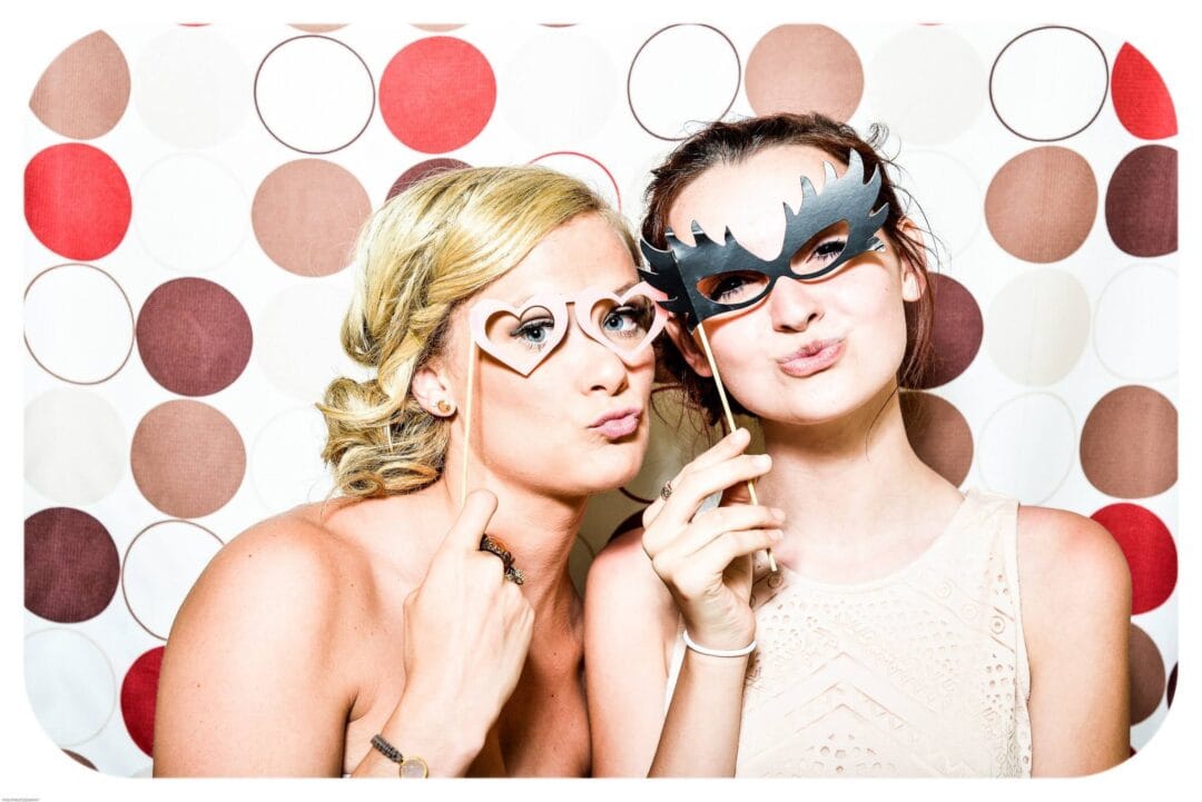 Two guests using an open-air photo booth hire with props and a patterned backdrop