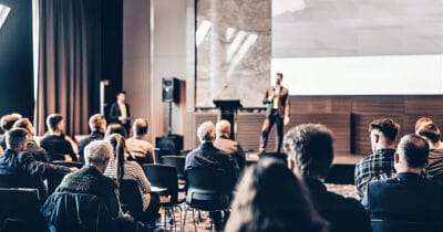 Conference audience seated while a speaker presents on stage at a corporate event venue