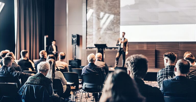 Conference audience seated while a speaker presents on stage at a corporate event venue