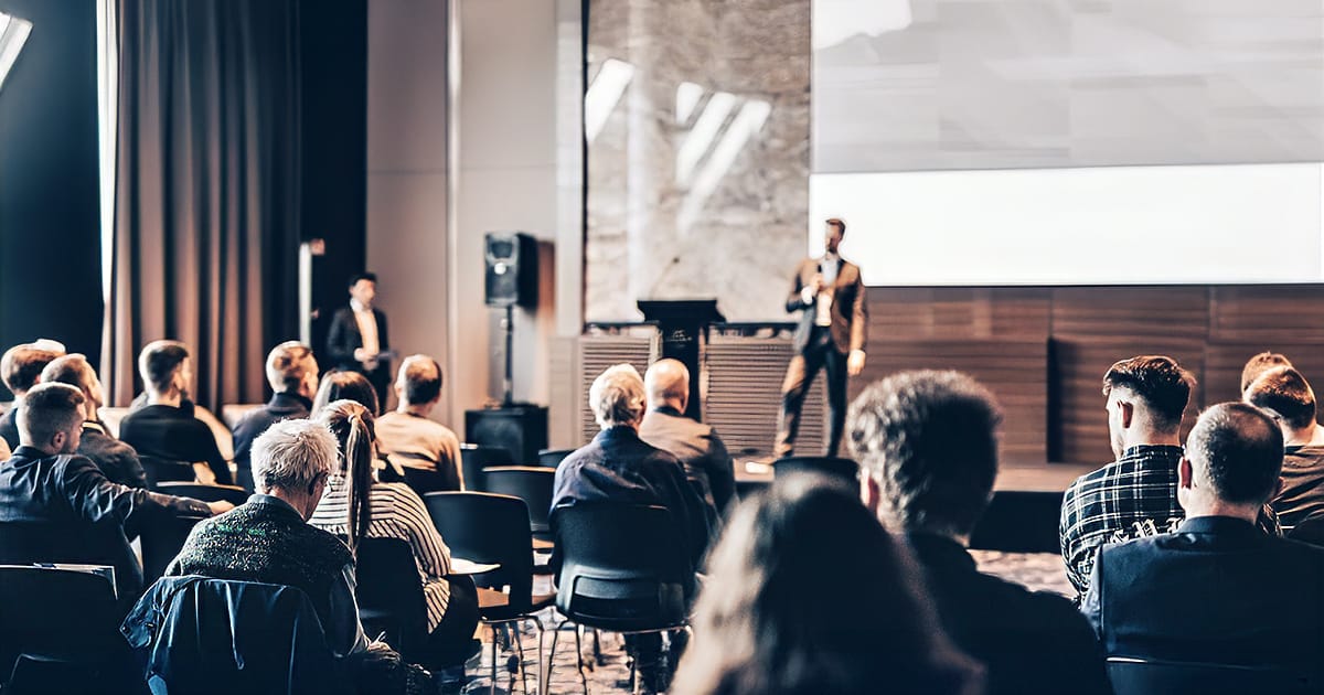 Conference audience seated while a speaker presents on stage at a corporate event venue